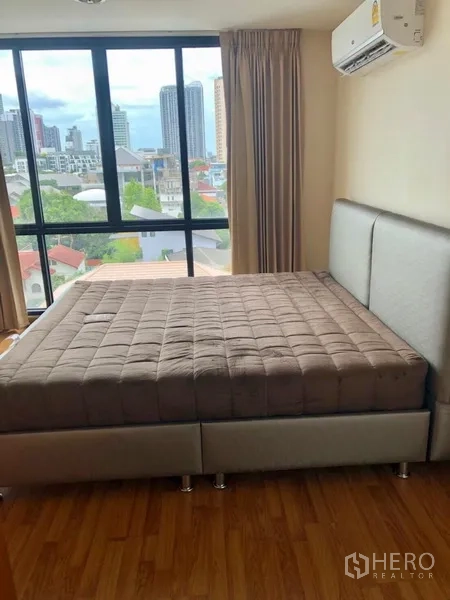 Condominium for rent in Watthana, Bangkok - Bedroom with large window, city view and air conditioner in a Watthana condominium.