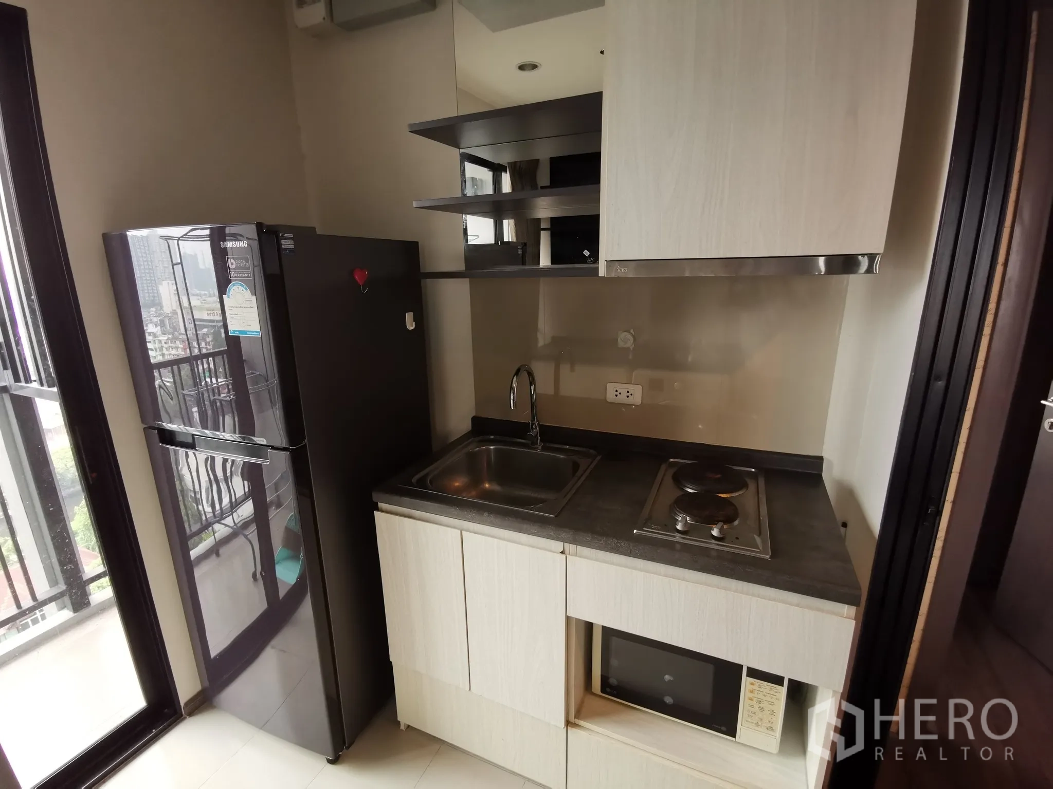 Condominium for rent or sale in Watthana, Bangkok - Compact kitchen with refrigerator, electric cooktop, sink and built-in microwave.