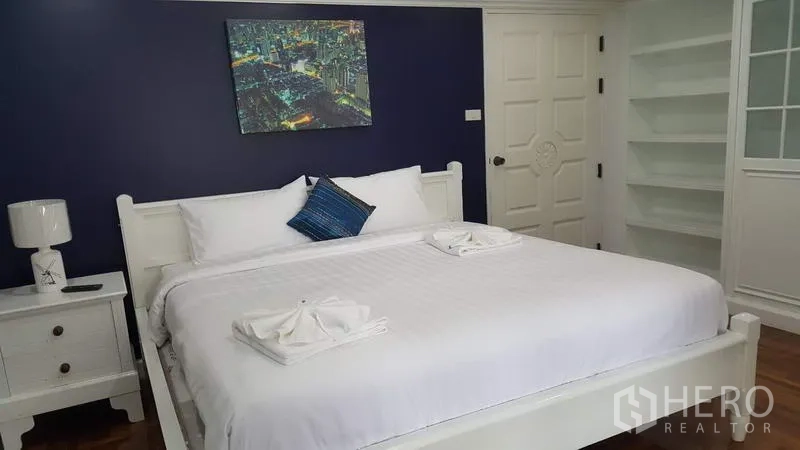 公寓 出租在Watthana, Bangkok - 温馨卧室，海军蓝特色墙，特大床与床头柜，开放式书架。