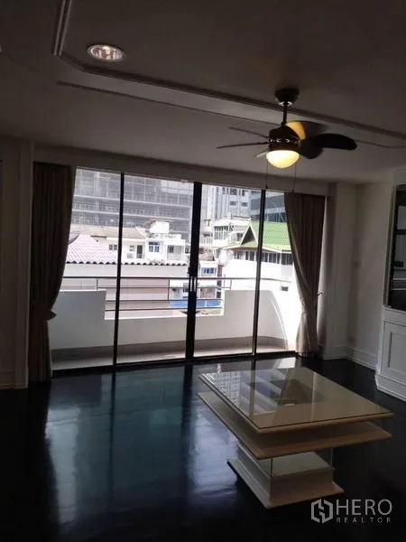 คอนโด ให้เช่าในSathon, Bangkok - ห้องนั่งเล่นมีพัดลมเพดาน โต๊ะกลาง และประตูกระจกเลื่อนไปยังระเบียงวิวเมือง