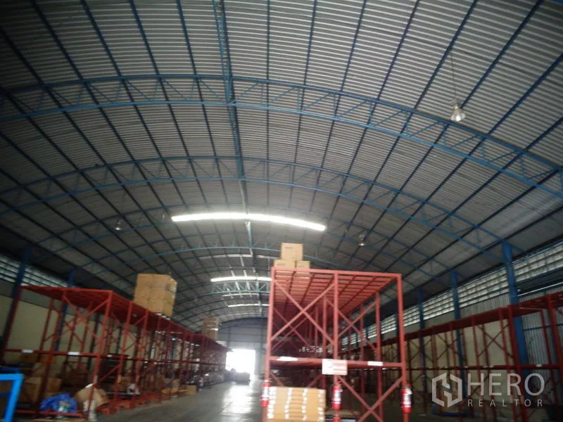 货栈 出租或出售在Lat Lum Kaeo, Pathum Thani - 弧形金属屋顶与蓝色桁架，上方为高大的红色存储货架。