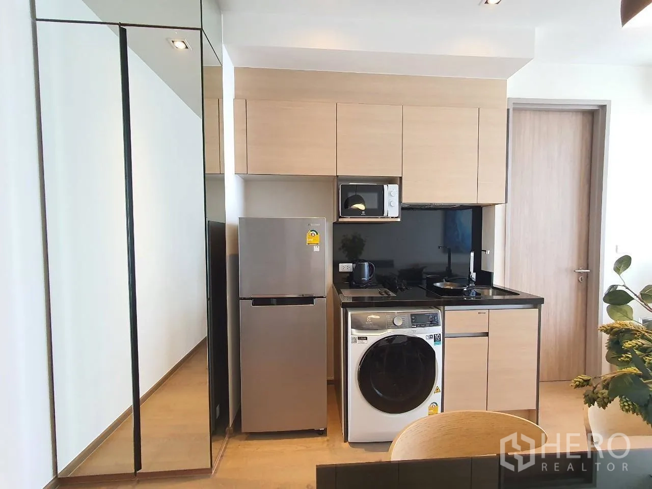 Condominium for rent in Khlong Toei, Bangkok - Compact modern kitchen with refrigerator, microwave, cooktop, and washing machine.