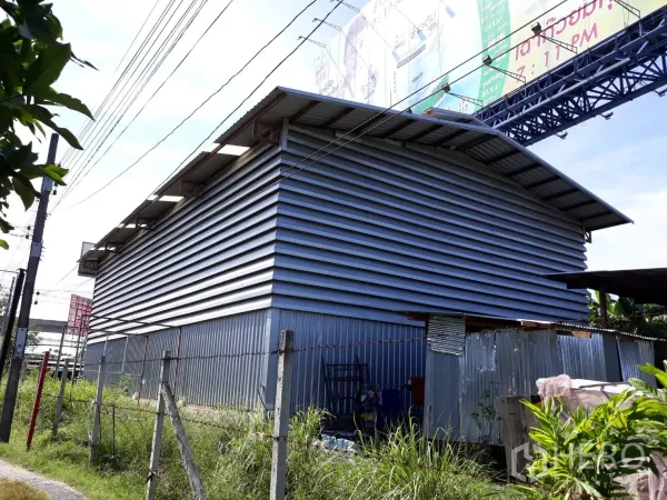 公寓 出租在Pathum Wan, Bangkok - 金属板外墙的人字顶建筑，旁有草地小路与围栏，高空电线经过。