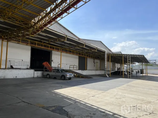 Warehouse for rent in Mueang Samut Prakan, Samut Prakan - Covered loading docks with ramps and a wide concrete yard at an industrial warehouse.