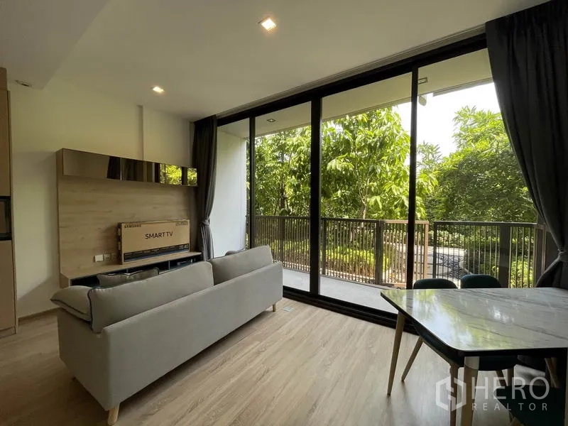 Condominium for sale in Watthana, Bangkok - Living area angle showing sliding glass doors to the balcony and lush greenery outside.