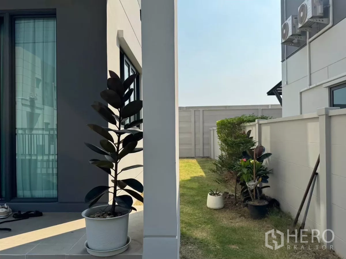 独立式住宅 出租在Bang Phli, Samut Prakan - 房屋侧院，草坪、盆栽与步道。