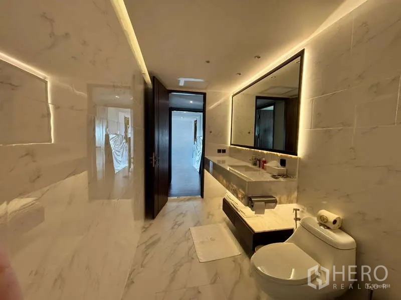 Condominium for rent in Watthana, Bangkok - Sleek marble bathroom with long vanity, illuminated mirror and toilet.