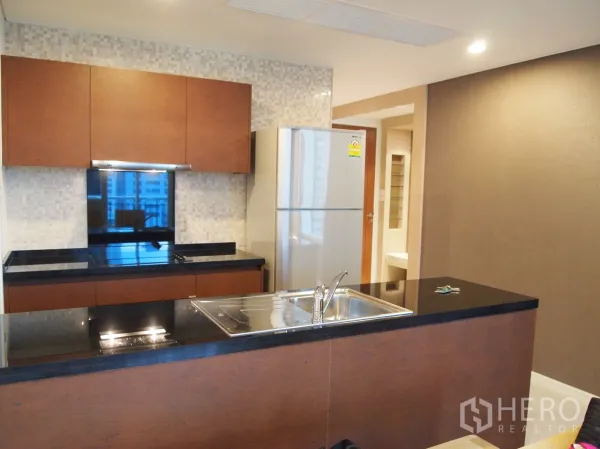 Condominium for rent or sale in Watthana, Bangkok - Modern open kitchen with black granite countertops, island sink and stainless fridge.