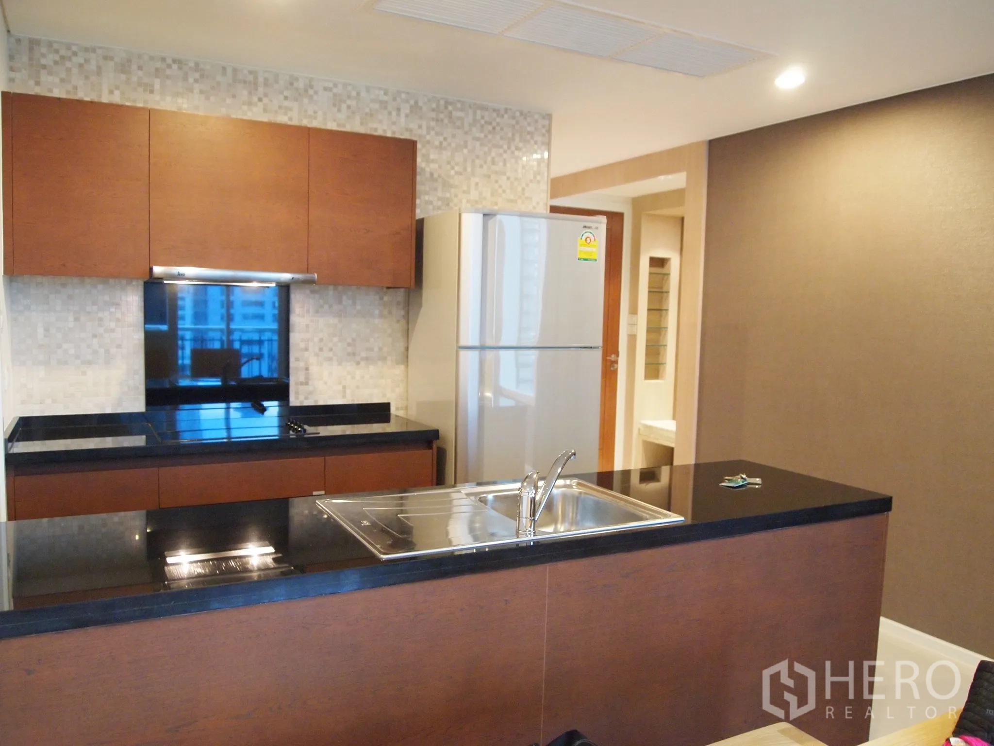 Condominium for rent or sale in Watthana, Bangkok - Modern open kitchen with black granite countertops, island sink and stainless fridge.