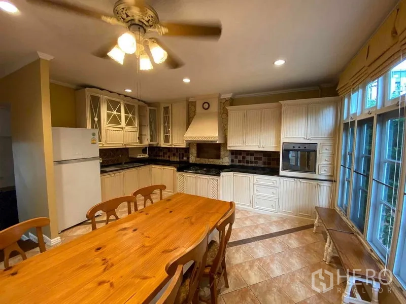 Townhouse for rent or sale in Mueang Samut Prakan, Samut Prakan - Country-style kitchen with white cabinetry, oven and long dining table.
