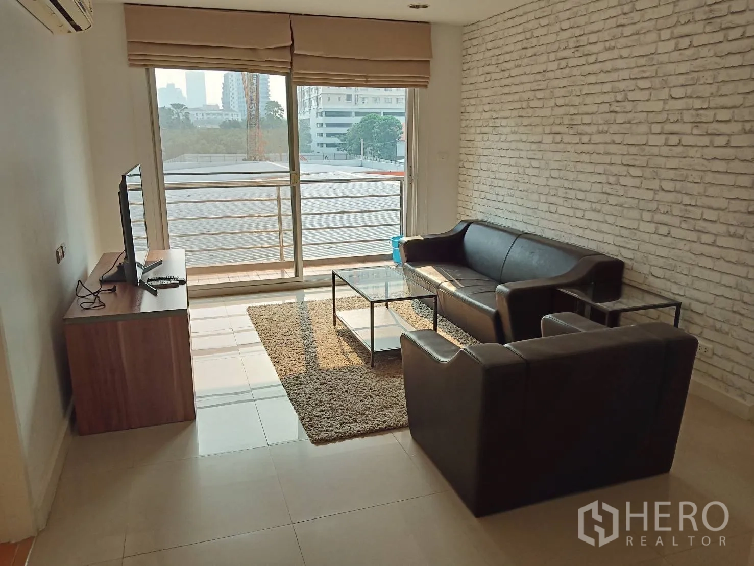 公寓 出租或出售在Khlong Toei, Bangkok - 客厅配黑色皮沙发、玻璃茶几和通往阳台的推拉门。
