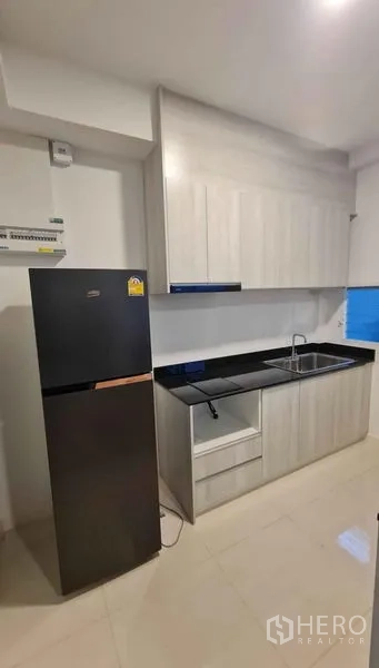 Townhouse for rent in Prawet, Bangkok - Fitted kitchen with black stone countertop, sink, ample cabinetry and a tall fridge.