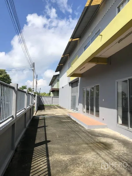 Factory for rent in Pathum Thani - Front loading and parking area with canopy, glass entries and roller shutter access.