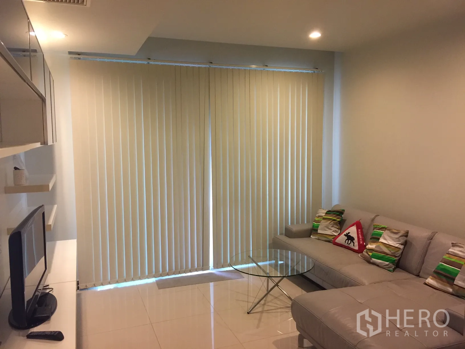 คอนโด ให้เช่าในWatthana, Bangkok - ห้องนั่งเล่นสว่าง โปร่ง ด้วยโซฟาเข้ามุม โต๊ะกลางกระจก ชั้นวางทีวี และม่านบังแสงสูงจรดเพดาน ในคอนโดใกล้ BTS นานา