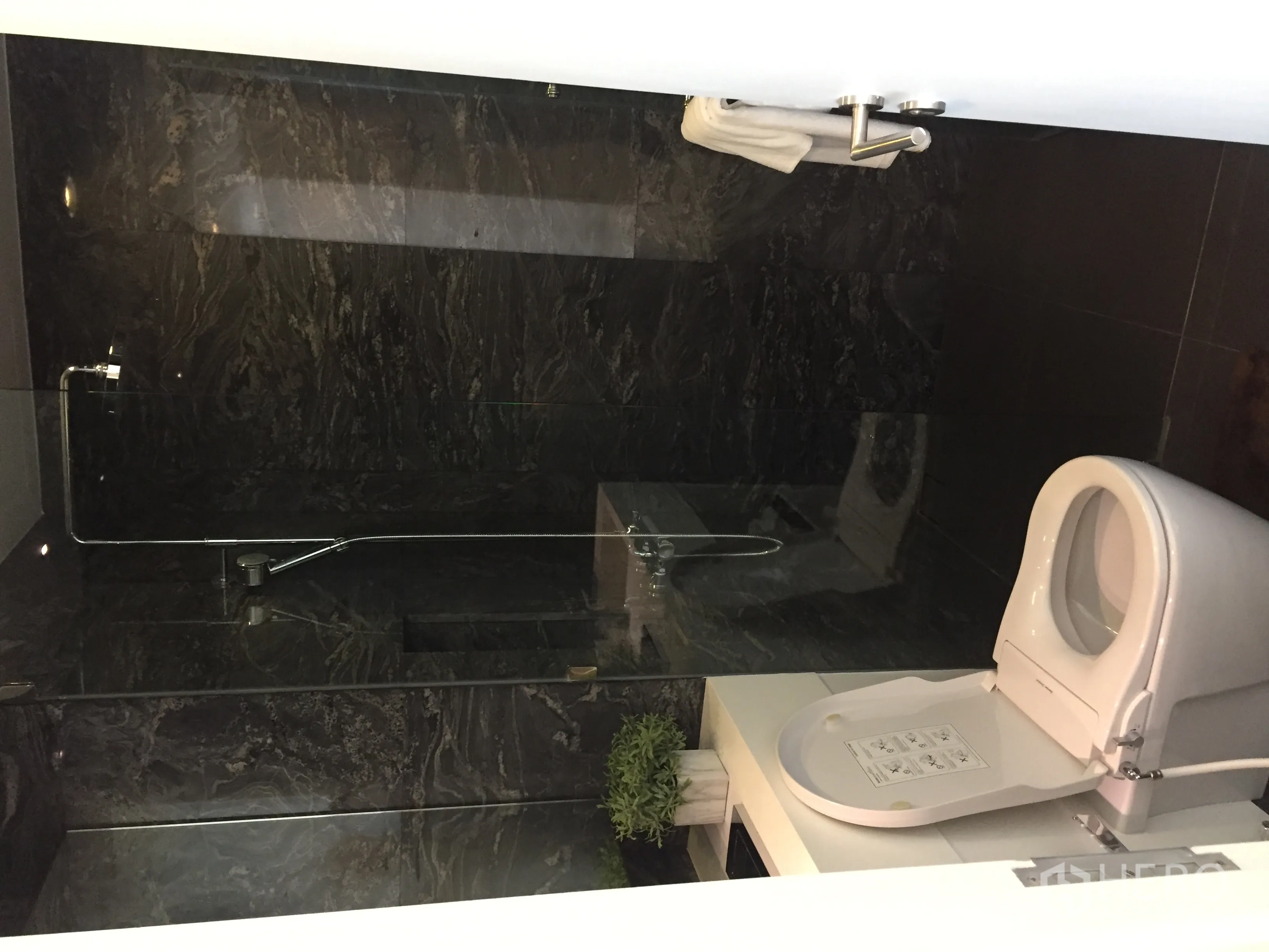 Condominium for sale in Bang Rak, Bangkok - Contemporary bathroom with dark stone tiles, glass shower and white fixtures.
