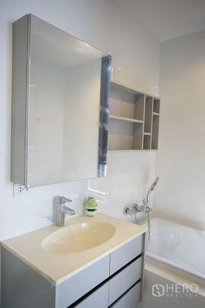 Condominium for rent in Watthana, Bangkok - Bathroom vanity with mirror cabinet, open shelves and bathtub faucet.