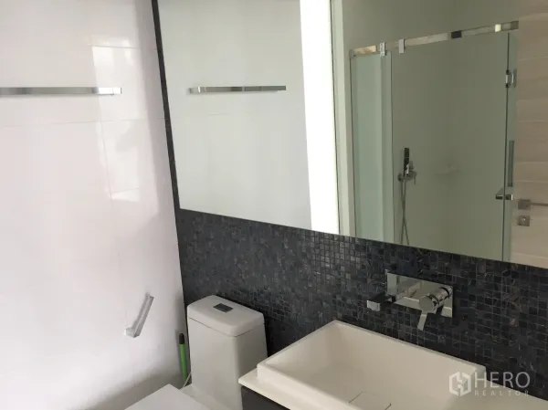 Condominium for rent in Bang Rak, Bangkok - Contemporary bathroom with a glass shower, large mirror, and mosaic tile backsplash.