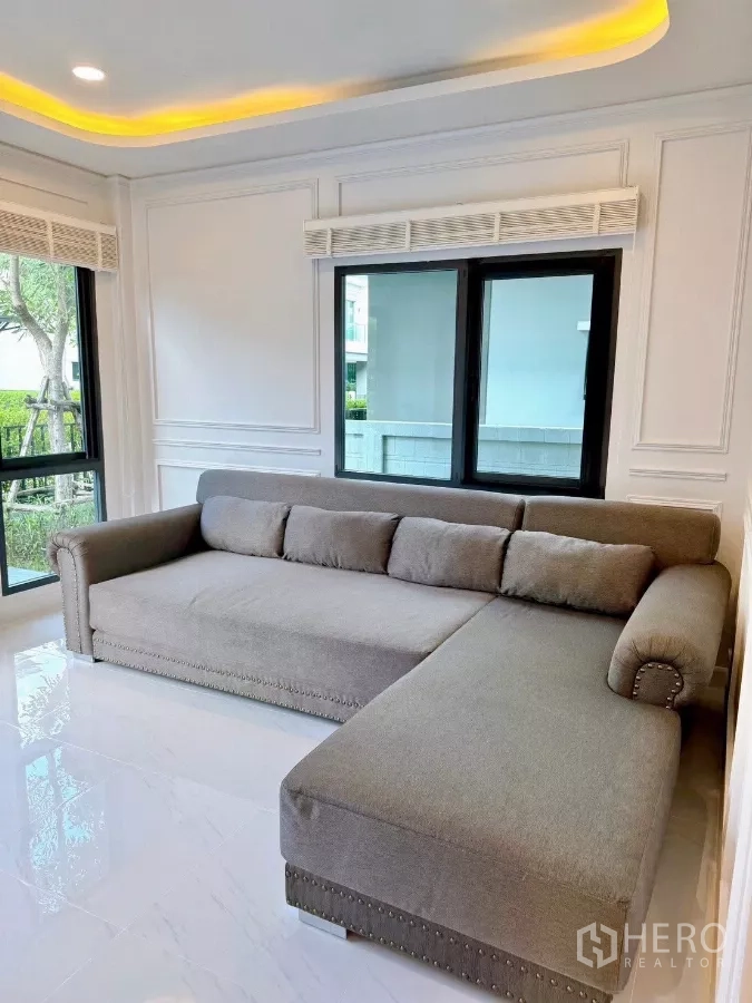 独立式住宅 出租在Bang Phli, Samut Prakan - 客厅一角，超大L形布艺沙发与窗边筒灯。