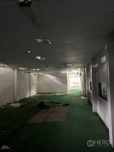 Warehouse for rent in Bang Kapi, Bangkok - Long warehouse hall with green floor and ceiling damage, daylight at the far end.