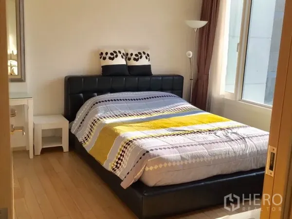 Condominium for rent in Khlong Toei, Bangkok - Cozy bedroom with padded bedframe, side tables and corner windows for natural light.