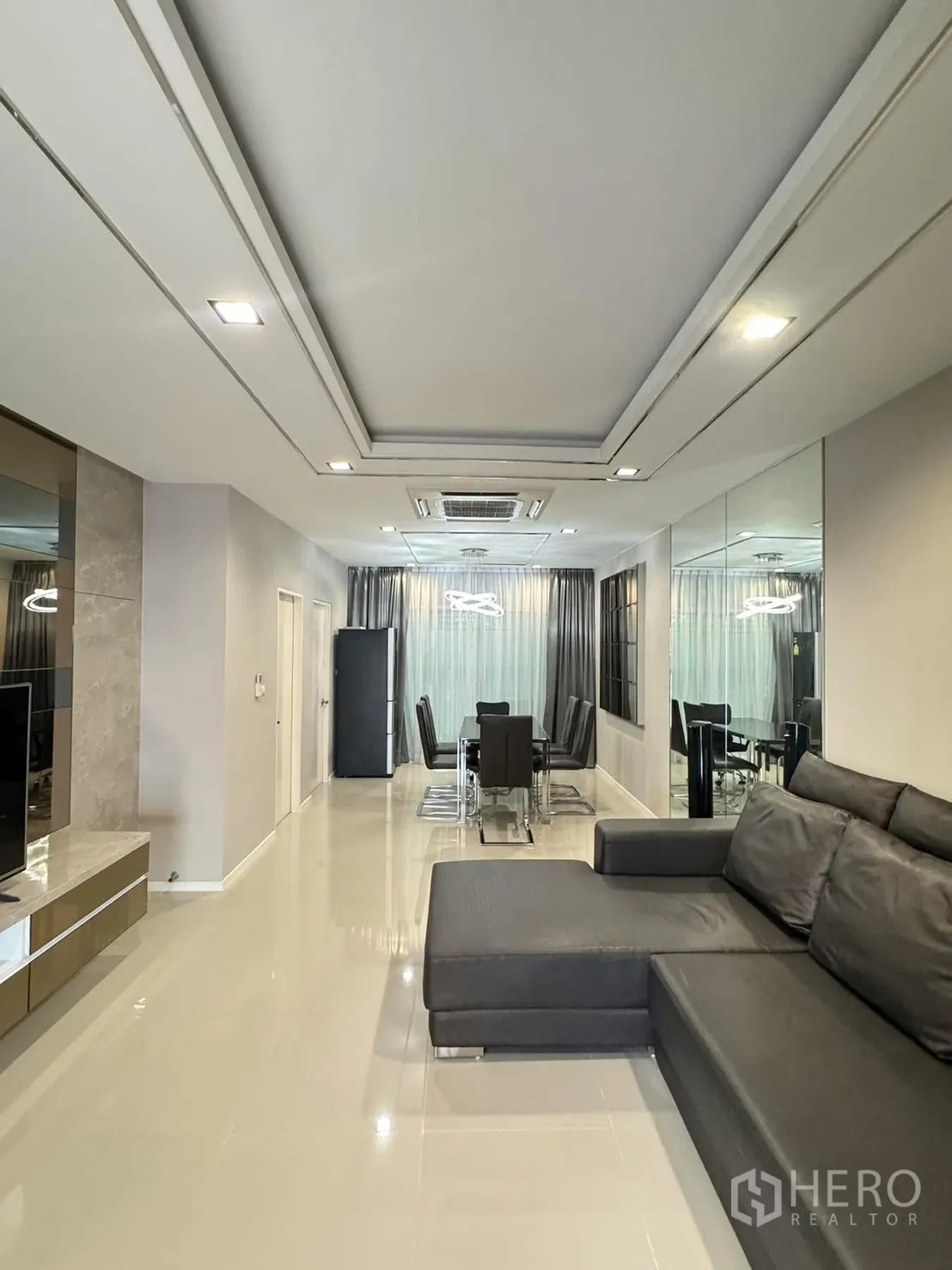 Townhouse for rent in Suan Luang, Bangkok - Open-plan living–dining room with L-shaped leather sofa and mirrored wall.