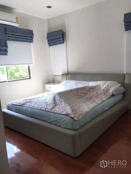 Detached House for sale in Saphan Sung, Bangkok - Cozy bedroom with large bed, corner windows and warm wood flooring.