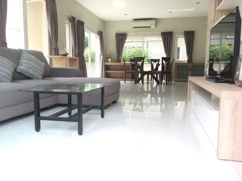 บ้าน ให้เช่าหรือขายในBang Na, Bangkok - ห้องนั่งเล่นและทานอาหารแบบโอเพนแปลน พร้อมโซฟาสีเทา โต๊ะกระจก และชั้นวางทีวี