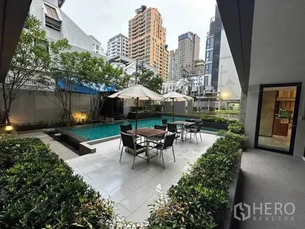 公寓 出租在Pathum Wan, Bangkok - 庭院式泳池配遮阳伞和座位，周围绿植与城市高楼景观。