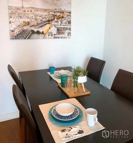 Condominium for rent in Khlong Toei, Bangkok - Dining table set for four with tableware and wall art on a white wall.