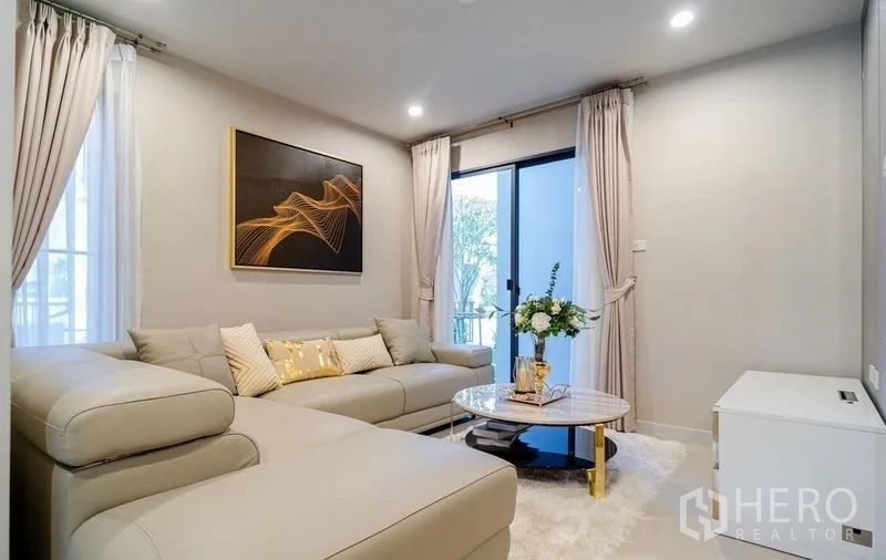 Detached House for sale in Lam Luk Ka, Pathum Thani - Another angle of the living area showing large windows, curtains, and a round marble coffee table.