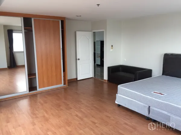 Condominium for rent in Khlong Toei, Bangkok - Spacious bedroom with wood flooring, mirrored sliding wardrobe and a small sofa.