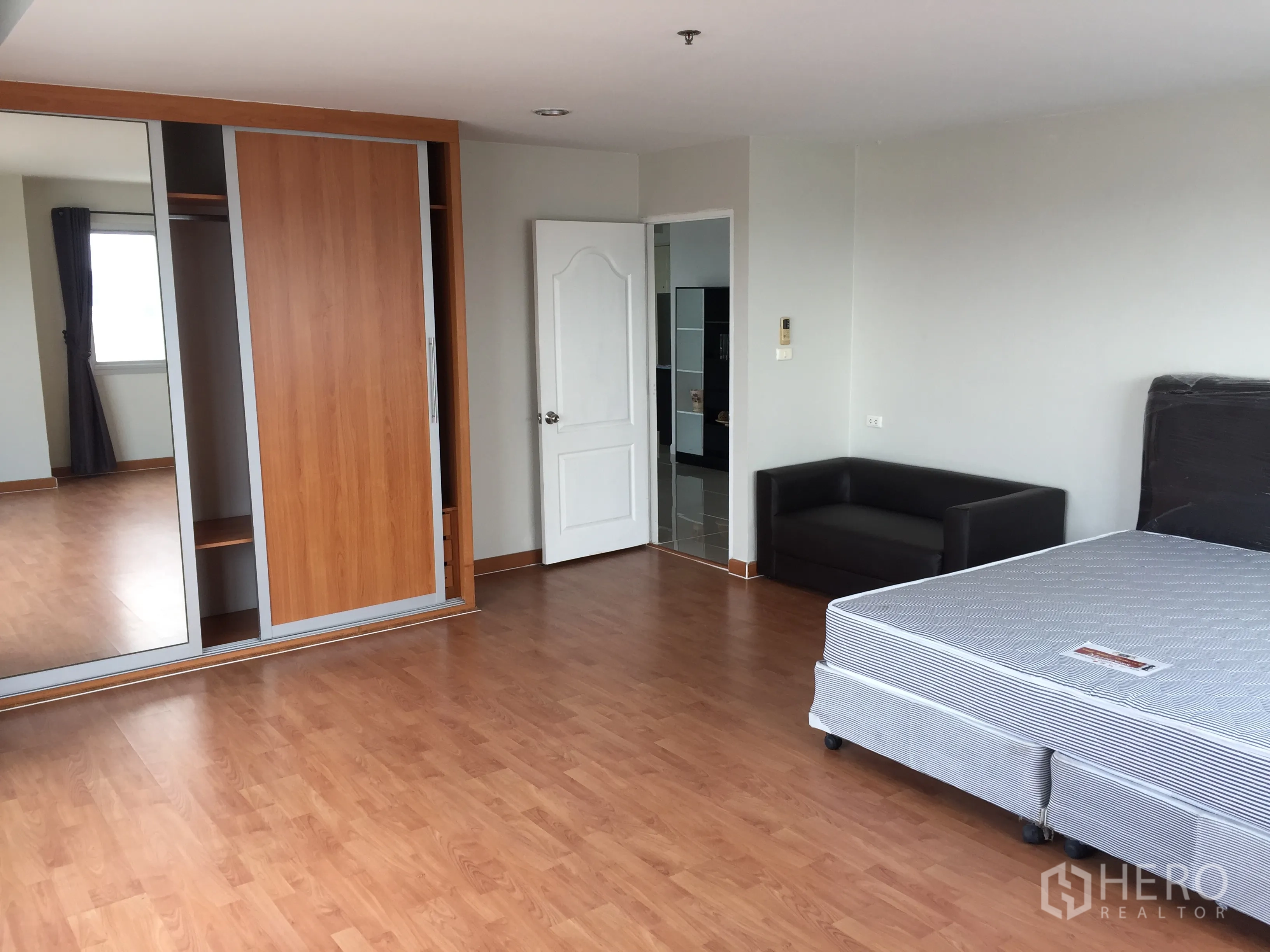 Condominium for rent in Khlong Toei, Bangkok - Spacious bedroom with wood flooring, mirrored sliding wardrobe and a small sofa.