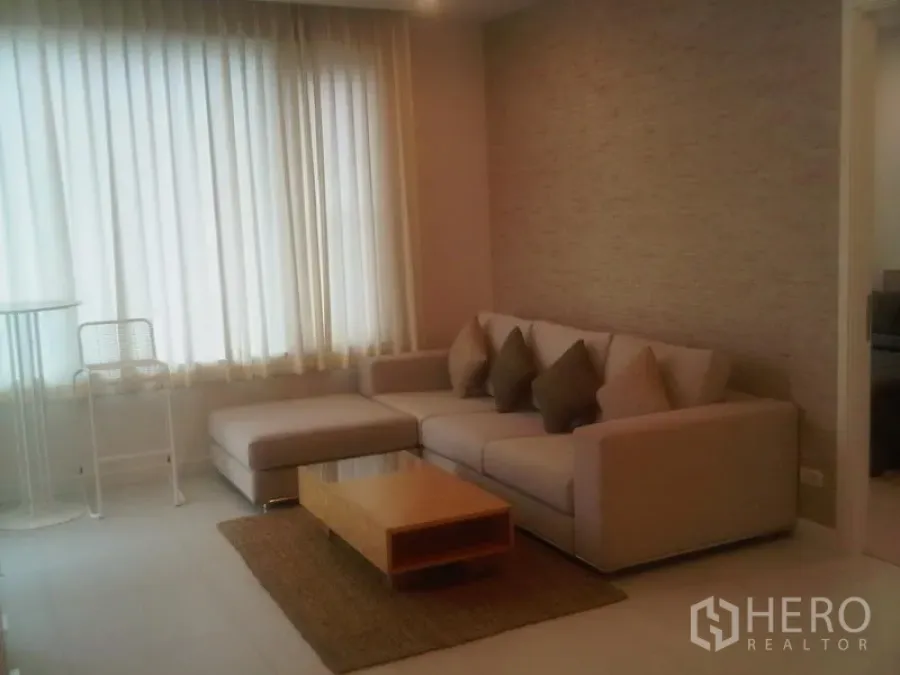 公寓 出售在Ratchathewi, Bangkok - 曼谷公寓客厅，L型沙发、茶几与落地窗薄纱窗帘，暖色调。
