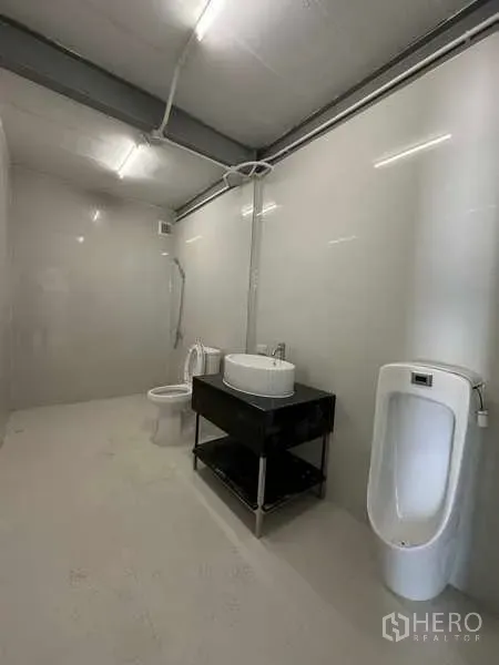 Factory for rent in Wang Noi, Phra Nakhon Si Ayutthaya - Clean restroom inside the factory featuring a toilet, urinal, and sink with bright lighting.