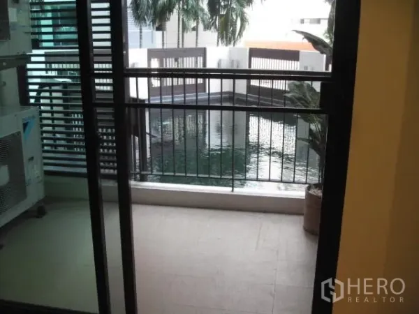 公寓 出租在Watthana, Bangkok - 推拉玻璃门外的阳台俯瞰泳池与棕榈景观。