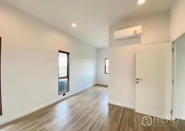 Detached House for sale in Bang Kapi, Bangkok - Bright bedroom with wood flooring, white walls, two windows and a wall-mounted air conditioner.