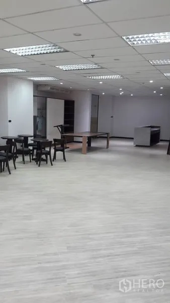 Office Space for rent in Huai Khwang, Bangkok - Spacious office floor with laminate flooring, fluorescent lighting, tables and a reception counter.