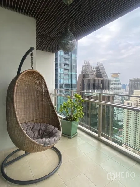 公寓 出租在Watthana, Bangkok - 有顶阳台，吊篮椅与盆栽，城市天际线为背景。