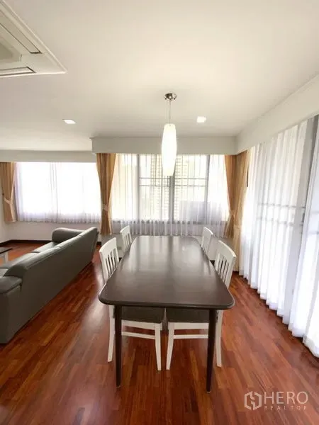 公寓 出租在Watthana, Bangkok - 餐区配四把白椅与吊灯，落地大窗配纱帘，光线明亮。