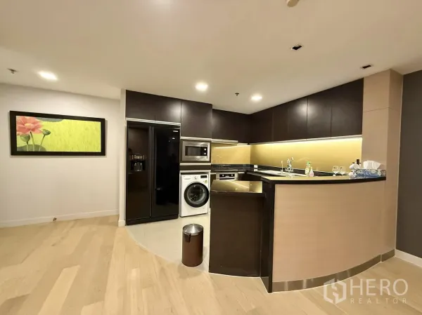 Condominium for rent or sale in Sathon, Bangkok - L-shaped modern kitchen with dark cabinetry, built-in appliances, washer, and under-cabinet lighting.