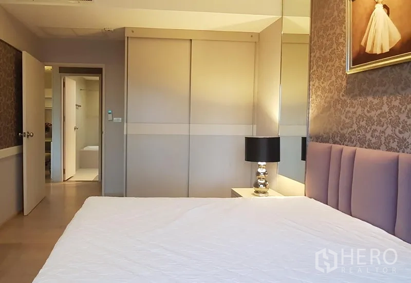 Condominium for rent in Khlong Toei, Bangkok - Cozy bedroom with padded headboard, sliding-door closet and doorway to an ensuite bathroom.