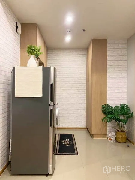 公寓 出售在Ratchathewi, Bangkok - 厨房走廊，双门冰箱、白色砖墙和绿植点缀。