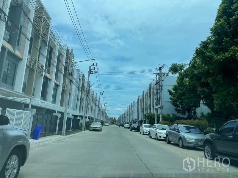 Townhouse for sale in Bueng Kum, Bangkok - Wide residential street lined with rows of contemporary townhouses and parked cars.