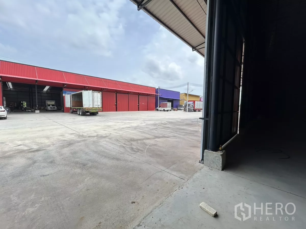 Warehouse for rent in Khlong Toei, Bangkok - View from inside the warehouse to a large loading yard with trucks and neighboring colorful warehouse bays.