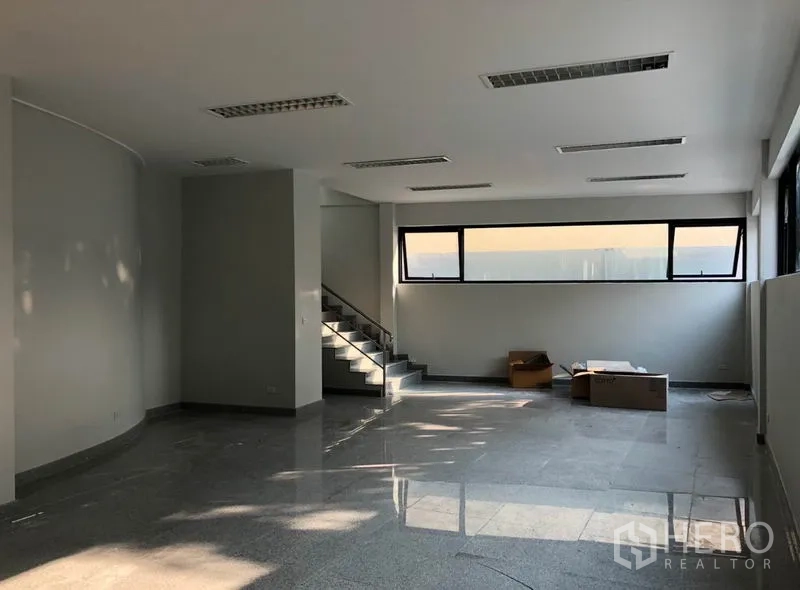 Office Space for rent in Khlong Toei, Bangkok - Open-plan office interior with polished stone flooring, a staircase, and long horizontal windows.