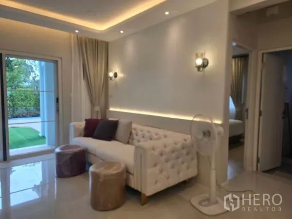独立式住宅 出租在Bang Phli, Samut Prakan - 休闲角落，纽扣沙发、壁灯与通往花园的移门。