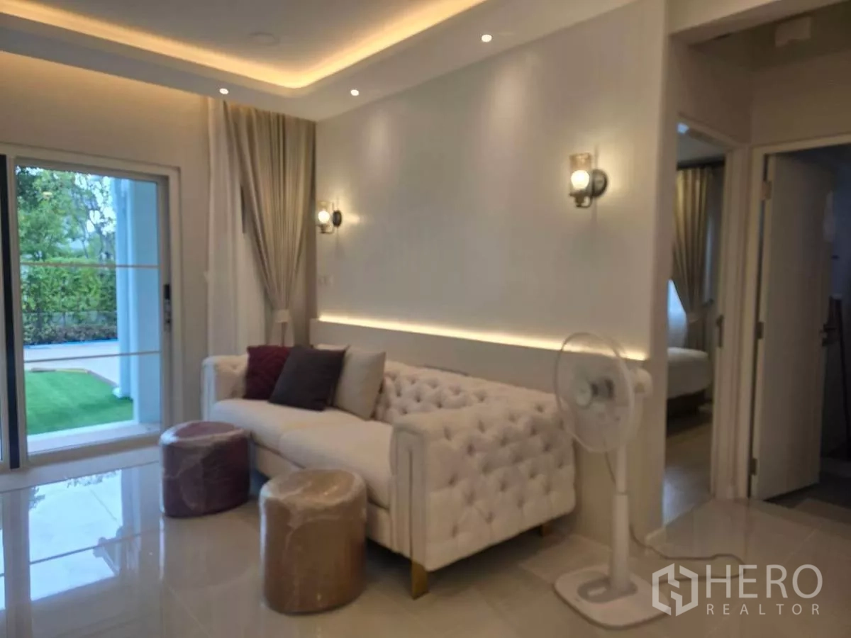 独立式住宅 出租在Bang Phli, Samut Prakan - 休闲角落，纽扣沙发、壁灯与通往花园的移门。
