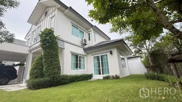 Detached House for rent in Bang Phli, Samut Prakan - Side view of the white two-storey house with large windows and a manicured lawn.