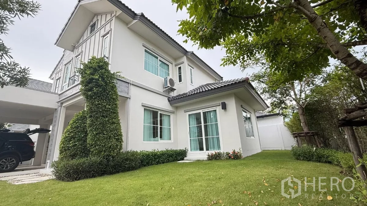 Detached House for rent in Bang Phli, Samut Prakan - Side view of the white two-storey house with large windows and a manicured lawn.