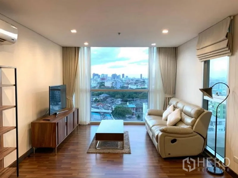 公寓 出租在Watthana, Bangkok - 明亮客厅，皮沙发与落地窗，可眺望曼谷城市景观。